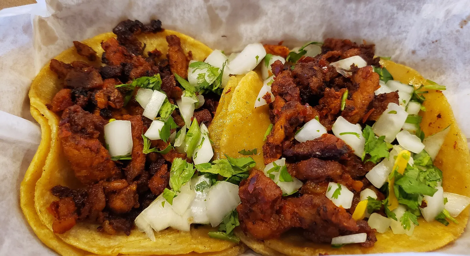 Adobada tacos with red chile-marinated pork, onion and cilantro on corn tortillas
