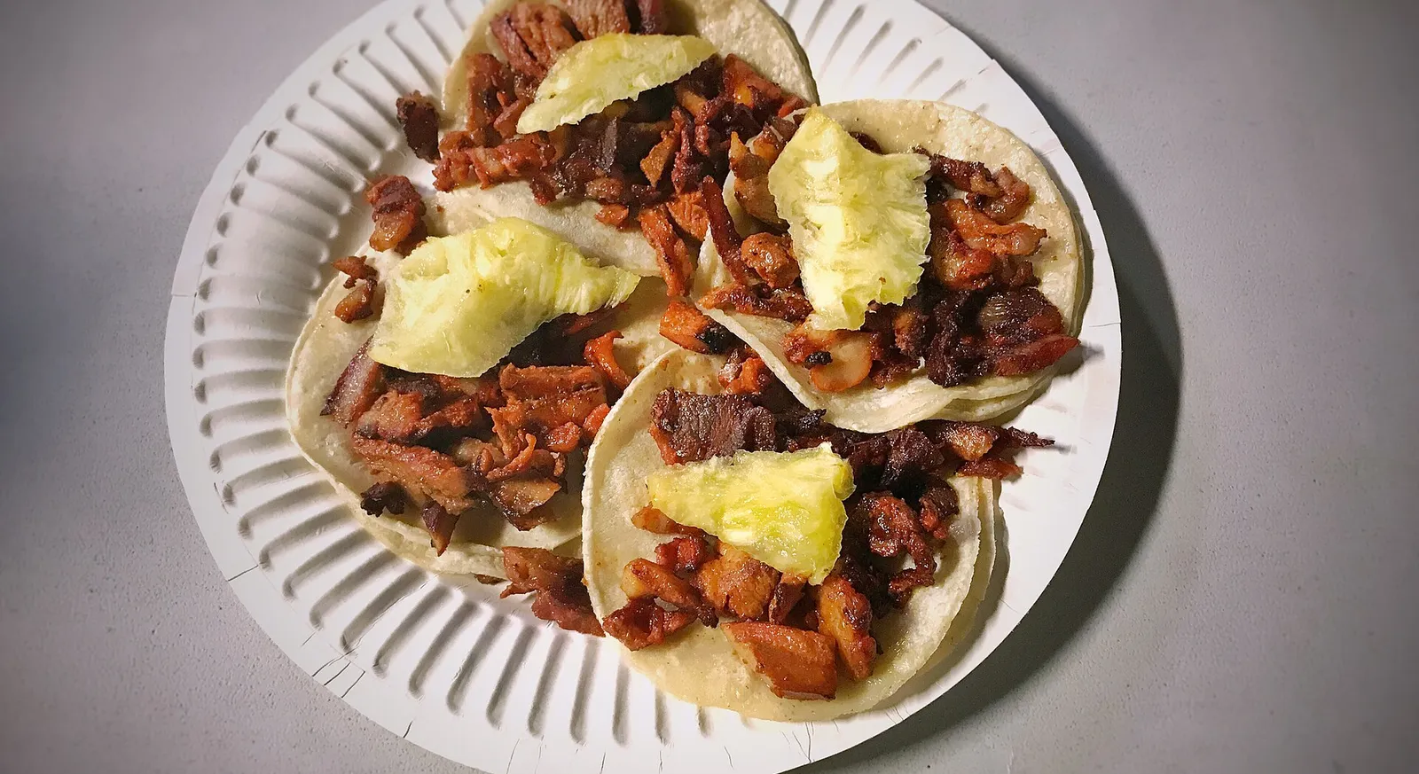 Al pastor tacos on corn tortillas topped with pineapple, onion and cilantro