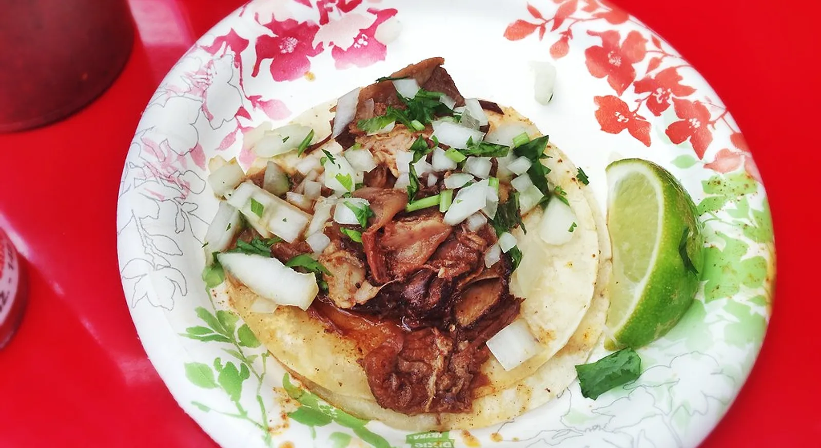 A birria taco with shredded stewed beef, onion, cilantro and lime