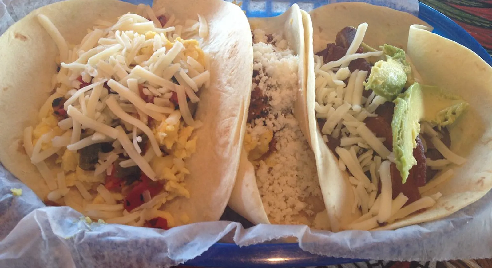 Breakfast tacos in flour tortillas filled with scrambled egg, shredded cheese and avocado, served in a paper-lined basket at Tacodeli in Texas