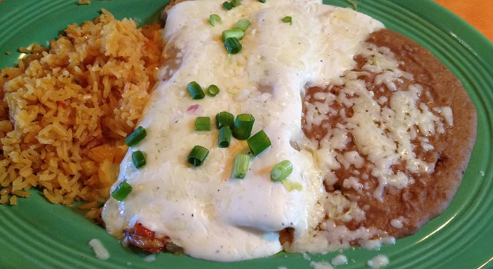 A plate of Mexican food: enchiladas in cream sauce with rice and refried beans