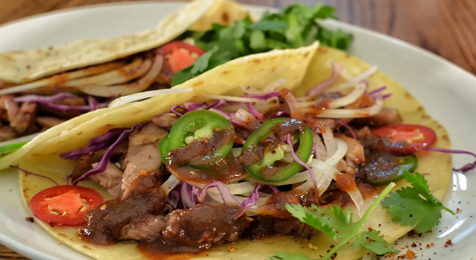 Pork tacos in soft tortillas with sliced jalapenos and slaw