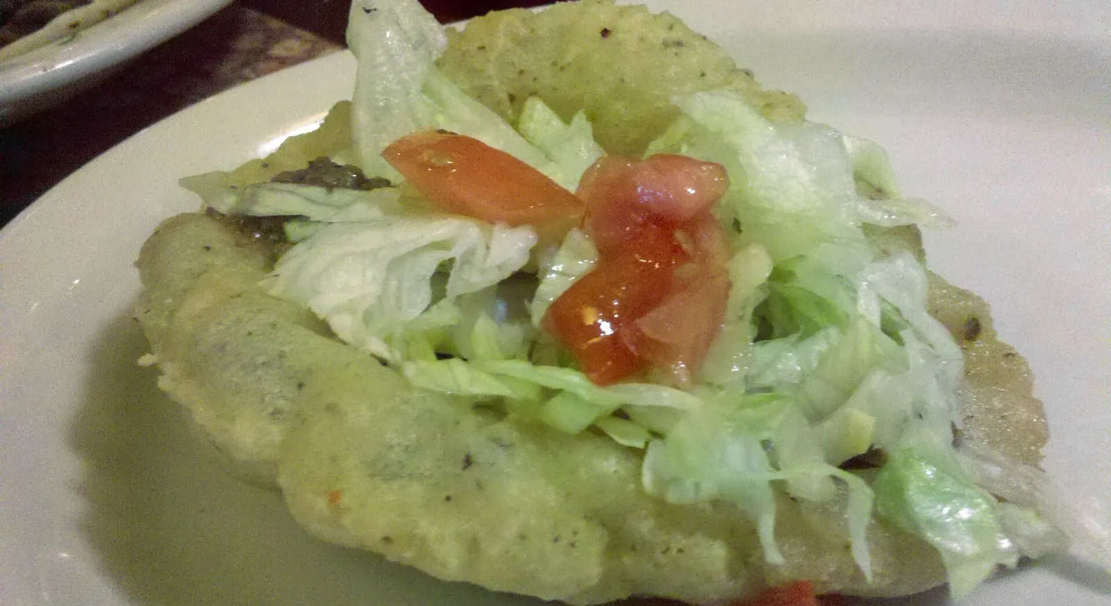 A puffy taco: a fried, puffed masa shell filled with meat, lettuce and tomato