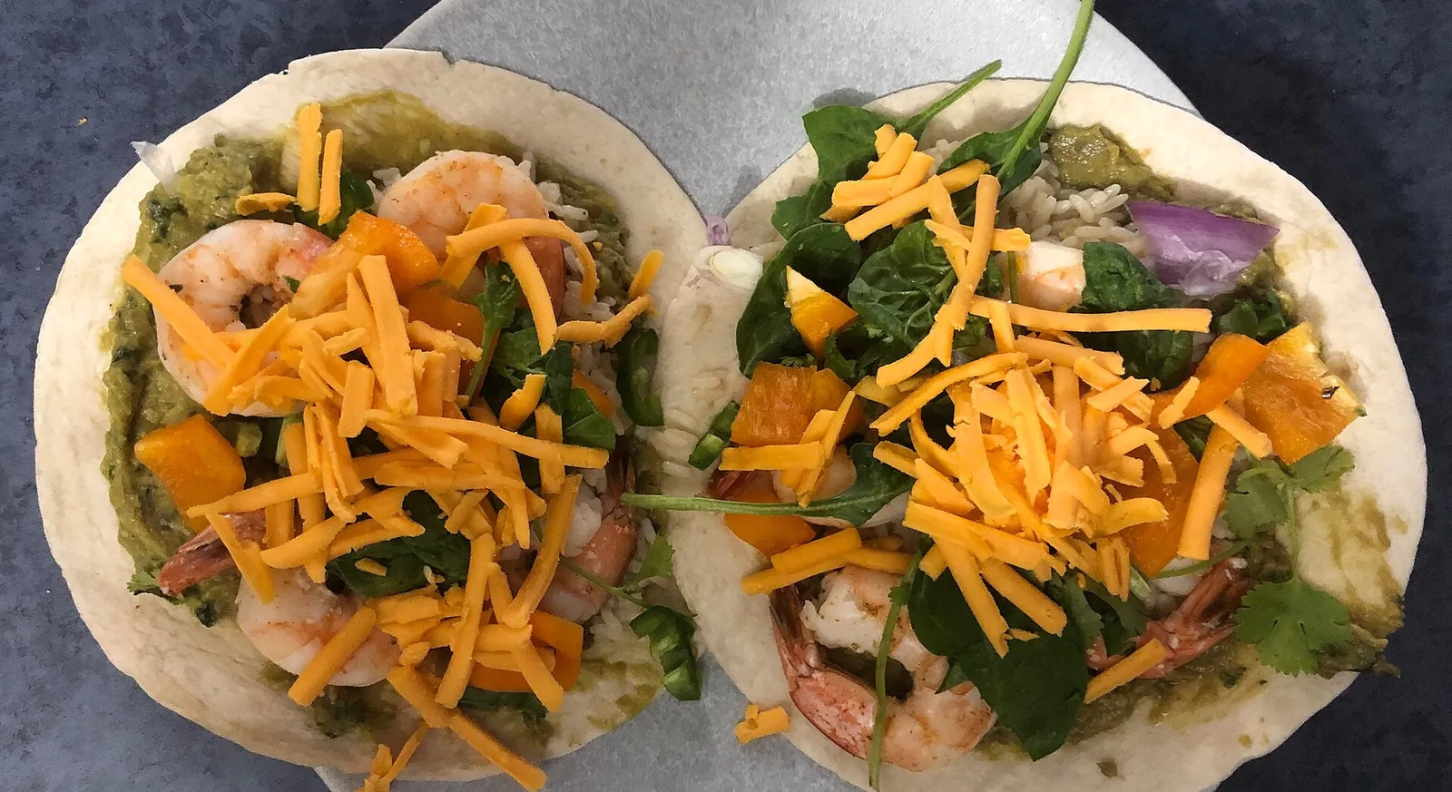 Two shrimp tacos (tacos de camaron) in flour tortillas with greens and shredded cheese