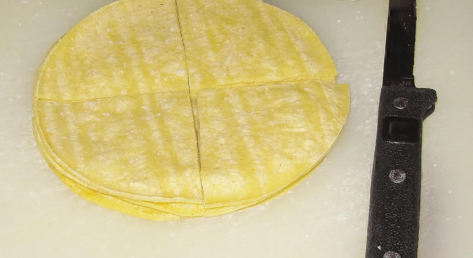 A stack of yellow corn tortillas cut into quarters on a board