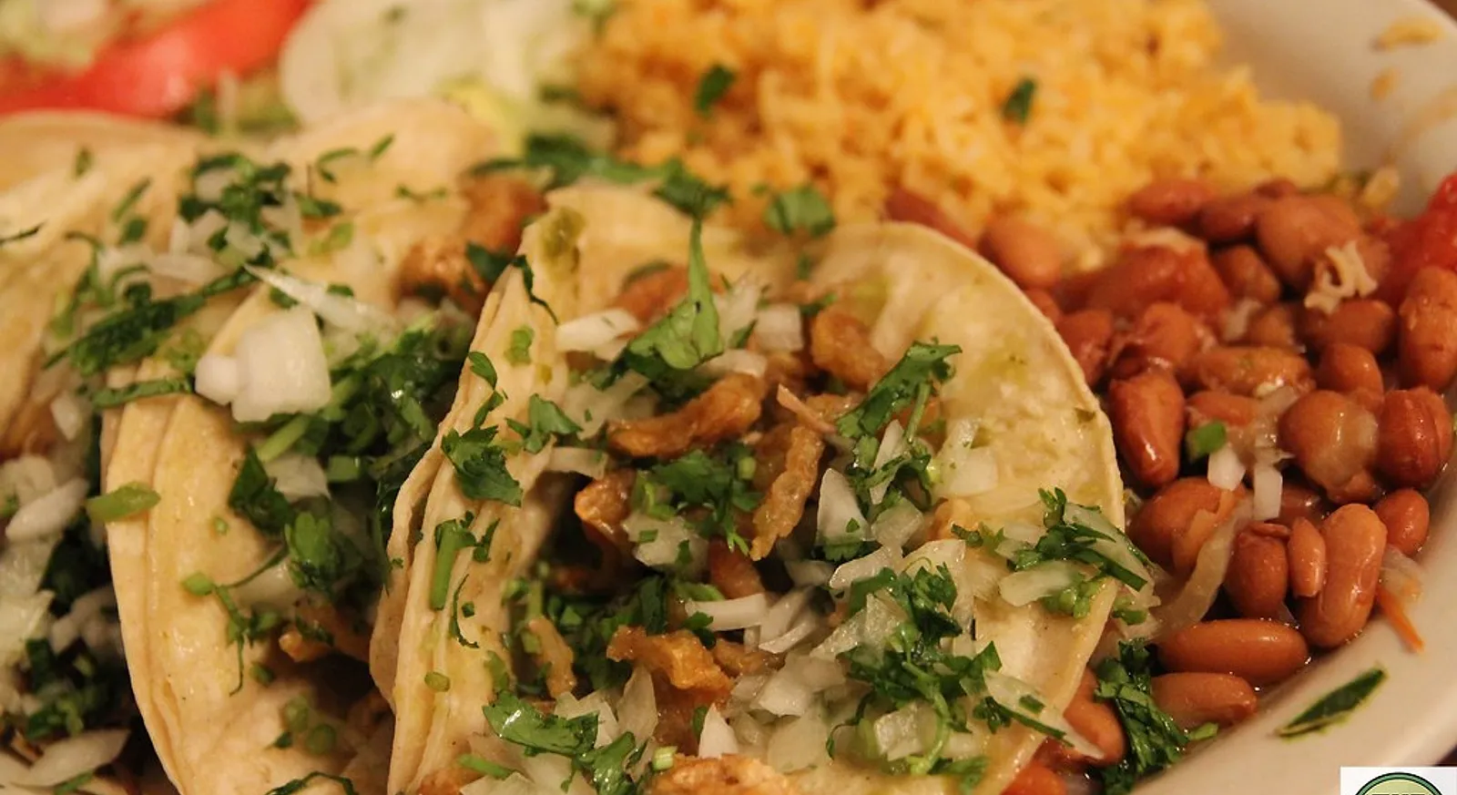 A taco platter with cilantro-topped tacos, rice and charro beans