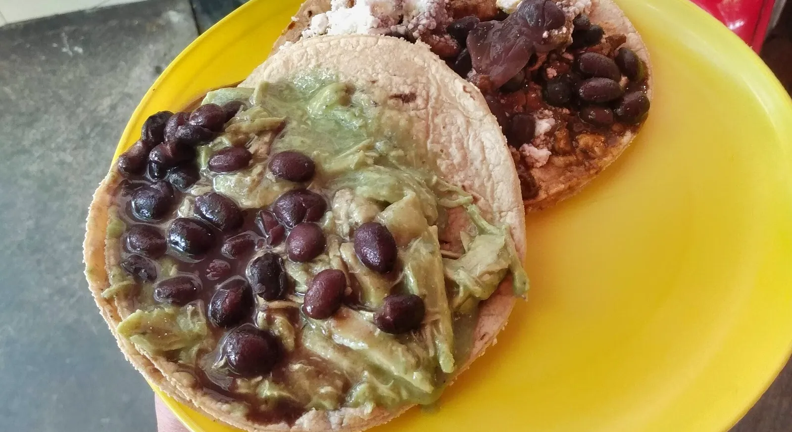Tacos de guisado topped with beans and stewed filling on a yellow plate