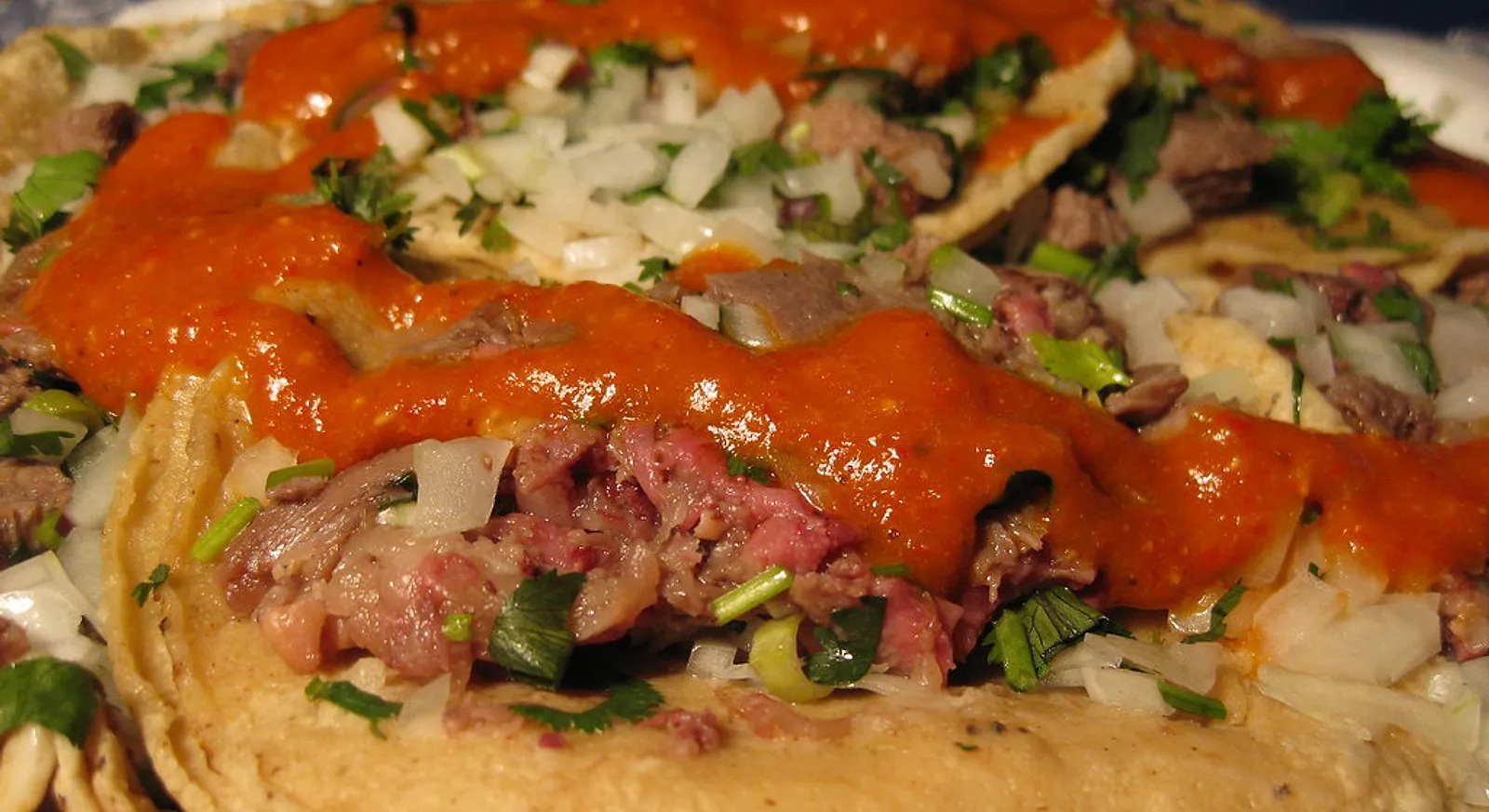 Tacos de lengua (beef tongue) covered in salsa roja with onion and cilantro