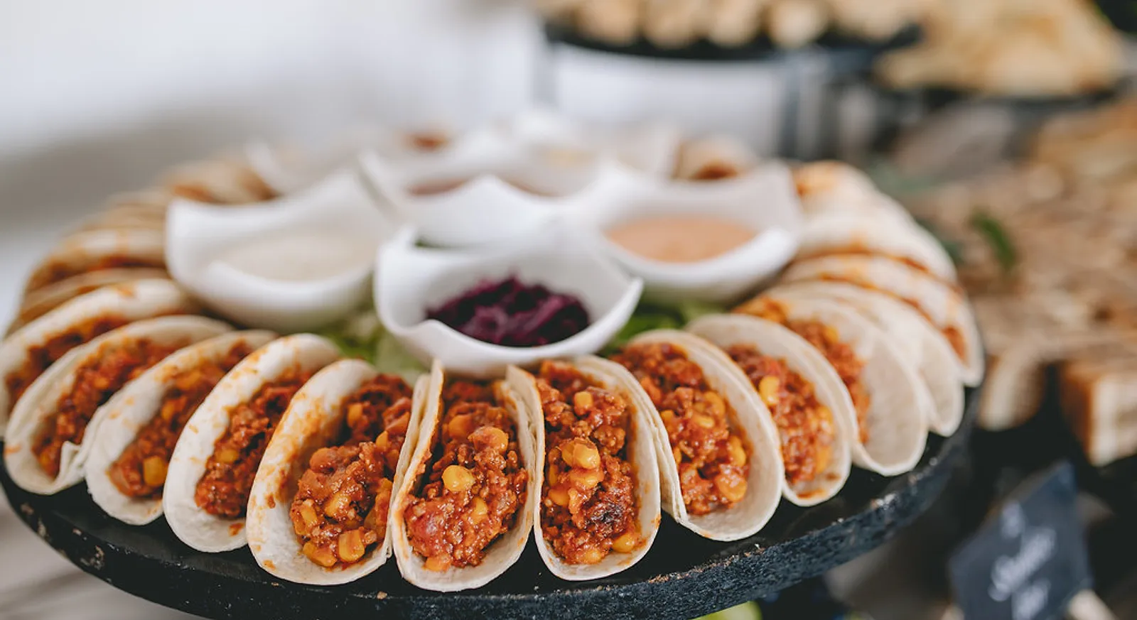 A round platter of tacos around bowls of dips, set out for a group